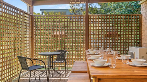 An outdoor dining area with a wooden table and chairs, surrounded by a bamboo fence.