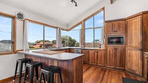 A modern kitchen with wooden cabinets, a large island with stools, a built-in microwave, and large windows offering a view of the neighborhood.