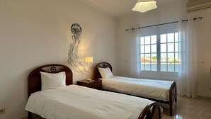 Ein Hotelzimmer mit zwei Einzelbetten, einem Nachttisch mit Lampe, einem Wandbild und einem Fenster mit Vorhängen.