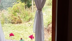 Una finestra con una tenda bianca, una vasca da bagno piena di bolle e fiori rosa sul davanzale.