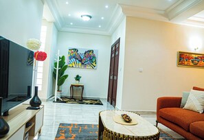 A living room with a TV, sofa, coffee table, and artwork on the walls. - Modern Chic Apartment Yaoundé  (Yaoundé)