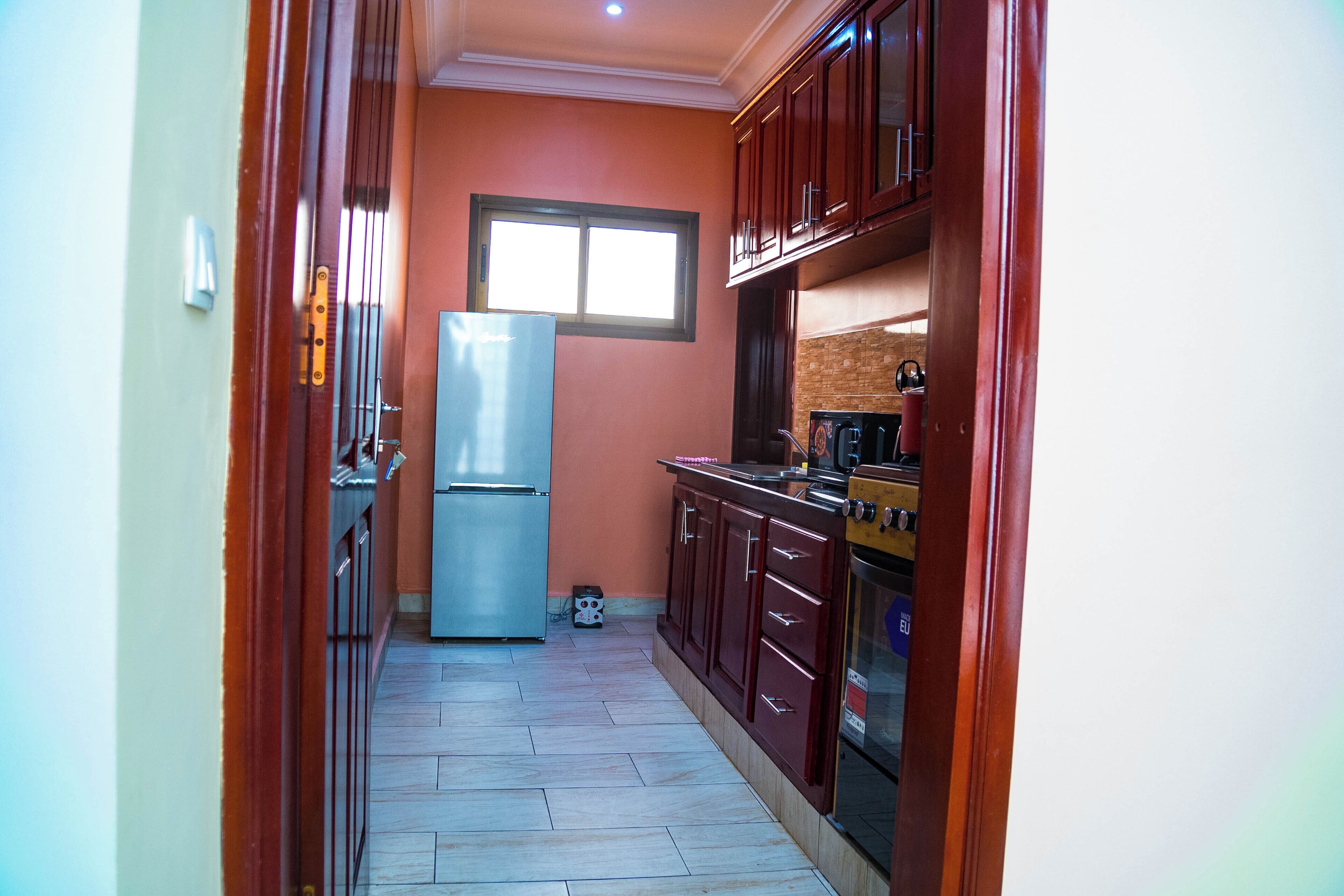 A narrow kitchen with wooden cabinets, a stainless steel refrigerator, and a stove.