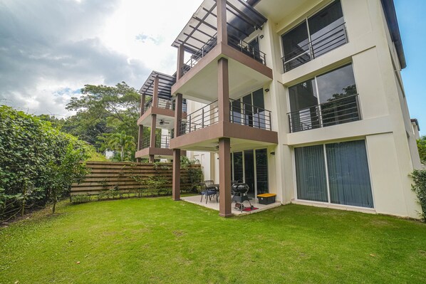 A modern multi-story building with balconies, a covered patio, and a well-maintained lawn.