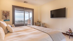 Une chambre avec un grand lit, un téléviseur fixé au mur, une fenêtre donnant sur un beau paysage et une petite table avec une chaise.