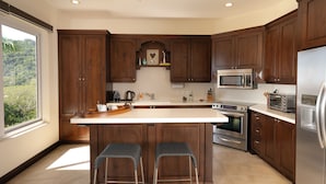 Une cuisine moderne avec des meubles en bois foncé, un îlot central doté de tabourets, des appareils électroménagers en acier inoxydable et une vue sur la verdure grâce à une grande fenêtre.