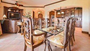 Un vaste espace dédié à la salle à manger, avec une table à plateau de verre entourée de chaises en bois richement décorées.