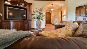 Un salon doté d’un grand téléviseur à écran plat, d’un canapé en cuir, d’un vase décoratif et d’une armoire en bois.
