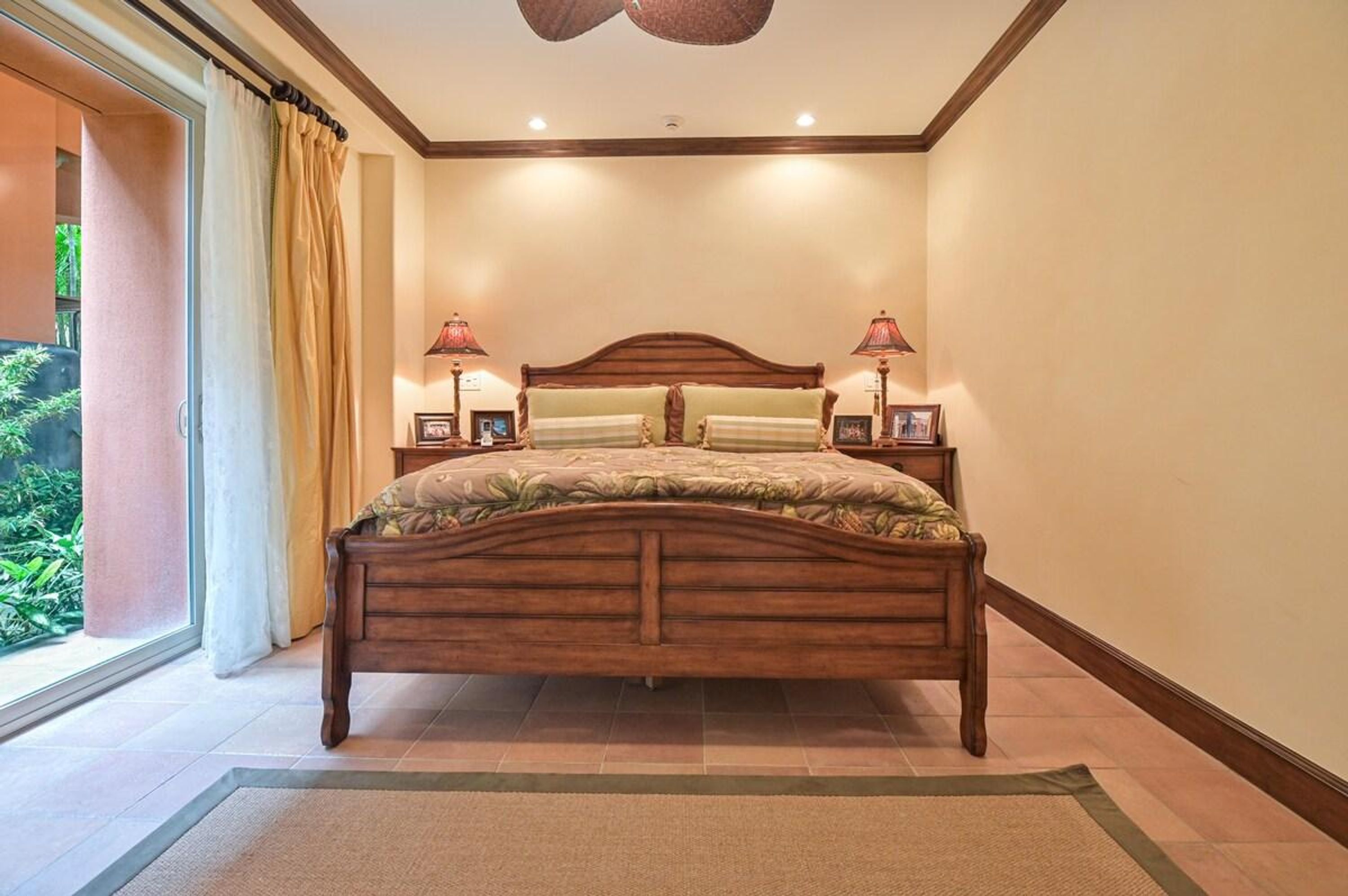 A bedroom with a wooden bed, two bedside lamps, and a view of greenery through a sliding door.