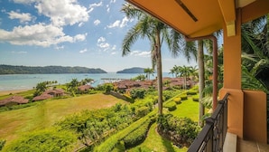 Un balcon avec vue sur une plage, des palmiers et une chaîne de montagnes lointaine.
