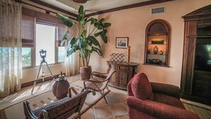 Un salon chaleureux avec une grande plante, des meubles en osier, un fauteuil rouge et une cheminée.