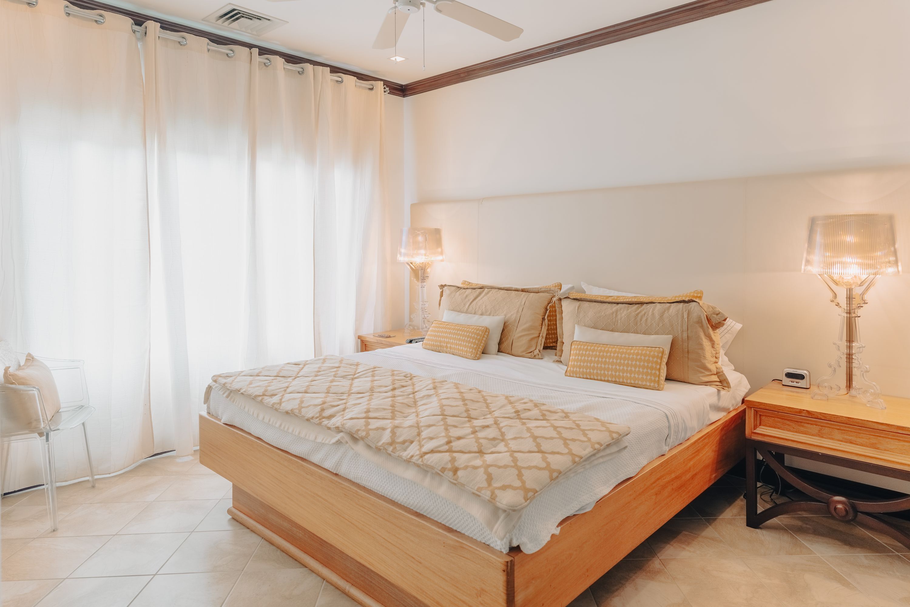 Un dormitorio con cama de madera, ropa de cama blanca, una mesita de noche con lámpara y una silla.