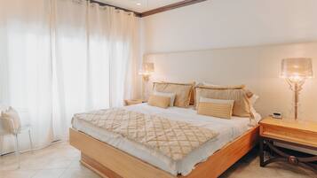 Un dormitorio con cama de madera, ropa de cama blanca, una mesita de noche con lámpara y una silla.