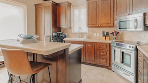 Una cocina con armarios de madera, horno de acero inoxidable, microondas, pileta y barra con un asiento.