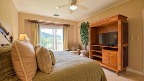 Un dormitorio con cama, mueble para televisión, ventilador de techo y vistas al exterior.