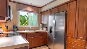 A modern kitchen with wooden cabinets, a stainless steel refrigerator, and a window with a view of palm trees. - CR Luxury Veranda 7B 2 Bdrm (Jacó)