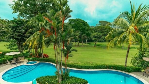 A swimming pool surrounded by lush greenery and palm trees, with a well-manicured lawn in the background. - CR Luxury Veranda 7B 2 Bdrm (Jacó)