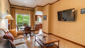 A living room with a sofa, coffee table, and TV. There's a dining area with chairs and a table. - CR Luxury Veranda 7B 2 Bdrm (Jacó)