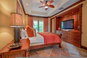 Un dormitorio con cama, televisor, ventilador de techo y un amplio ventanal.
