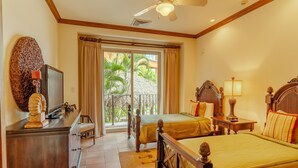 Habitación de hotel con dos camas, televisor, escritorio y balcón con vistas a palmeras.