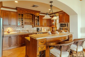 A spacious kitchen with wooden cabinets, a large island with bar stools, and a built-in microwave. - CR Luxury Montebello 1D 3 Bdrm (Jacó)