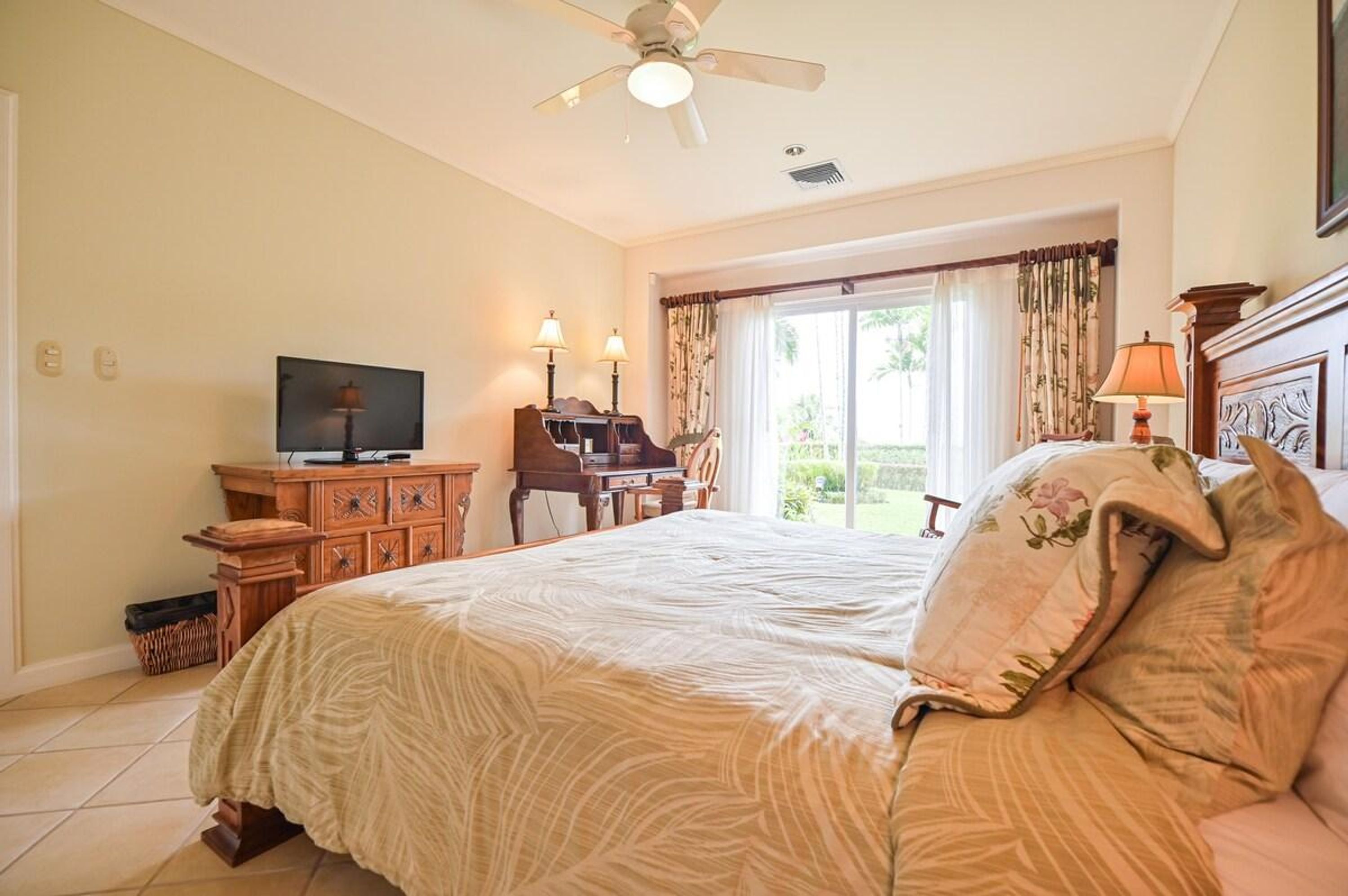 Een slaapkamer met een bed, een bureau met een computer, een televisie en een raam met gordijnen.