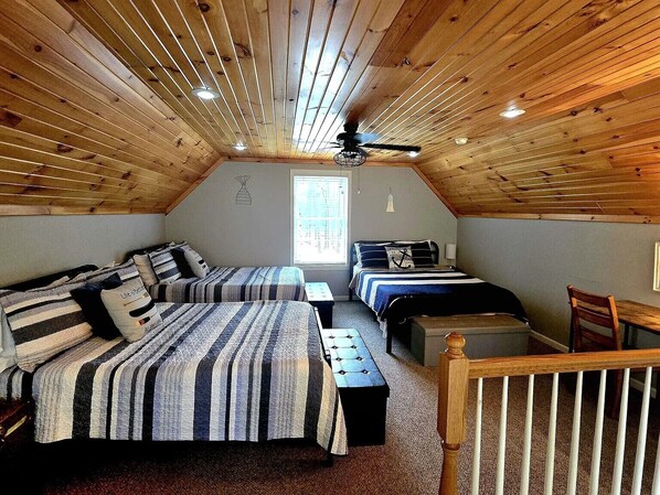 Une chambre mansardée chaleureuse avec deux lits, un ventilateur de plafond et une petite table.