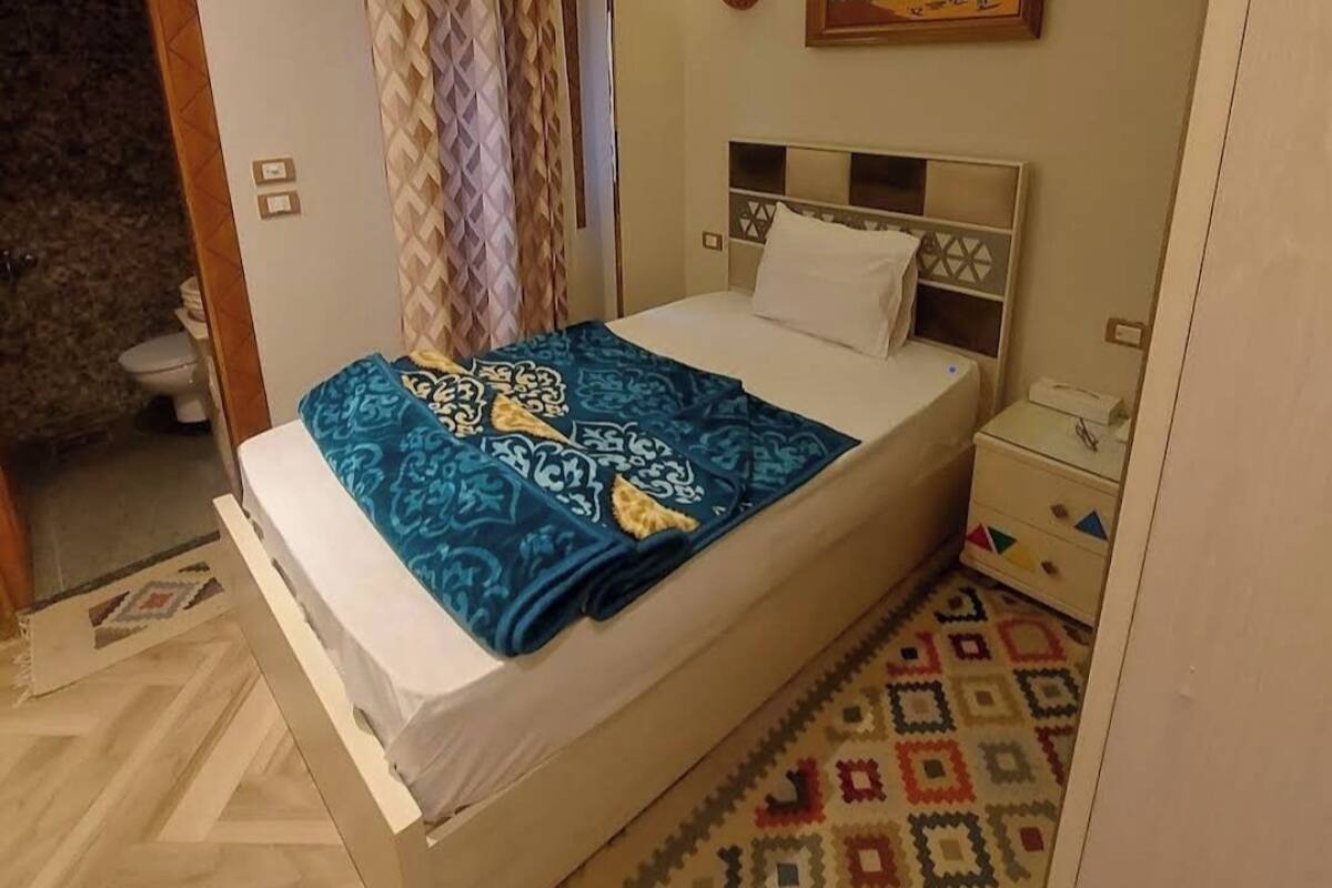 A bedroom with a bed, a nightstand, a bedside table, a wall-mounted air conditioner, a painting, and a patterned rug.
