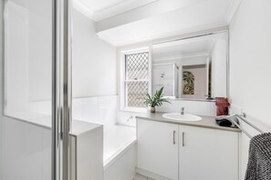 Bathroom features a bathtub, large mirror, and a potted plant.