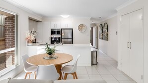 A modern kitchen with white cabinets, a central island, and a dining area with a round table and chairs. - Contemporary Chic on CBD Fringe! (Toowoomba)