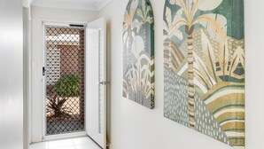 A hallway with a sliding glass door leading to a patio area, flanked by two large wall-mounted artworks depicting abstract plant designs. - Contemporary Chic on CBD Fringe! (Toowoomba)