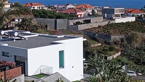A modern building with a flat roof, a small balcony, and a view of the sea. - Holiday House Caetano (PONTA DO SOL)
