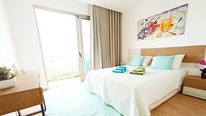 A modern hotel room with a large bed, a view through the sliding glass door, a painting on the wall, and a small table with a plant. - Holiday House Caetano (PONTA DO SOL)