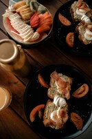 Una mesa con dos platos de comida, uno con frutas cortadas y otro con sándwiches cubiertos de tocino y crema.
