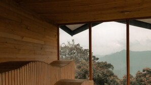 A wooden interior with a sloped ceiling and a view of a mountainous landscape through large windows. - Santuario Luxury Ecohotel (Villeta)