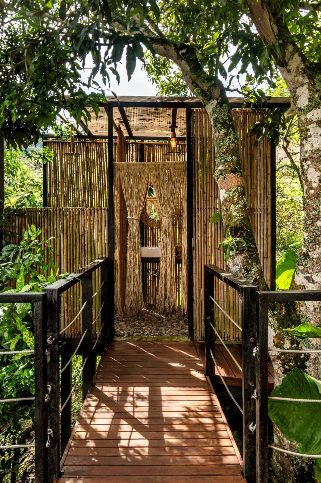 Un puente de madera que conduce a un portón de bambú con una lámpara colgante.