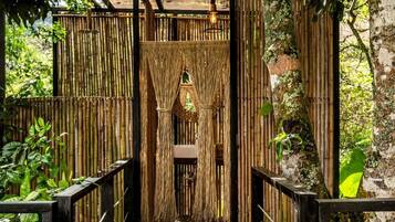 Un puente de madera que conduce a un portón de bambú con una lámpara colgante.