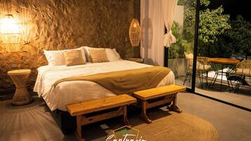 A bedroom with a large bed, bedside tables, a bench, and a view of the outdoors.