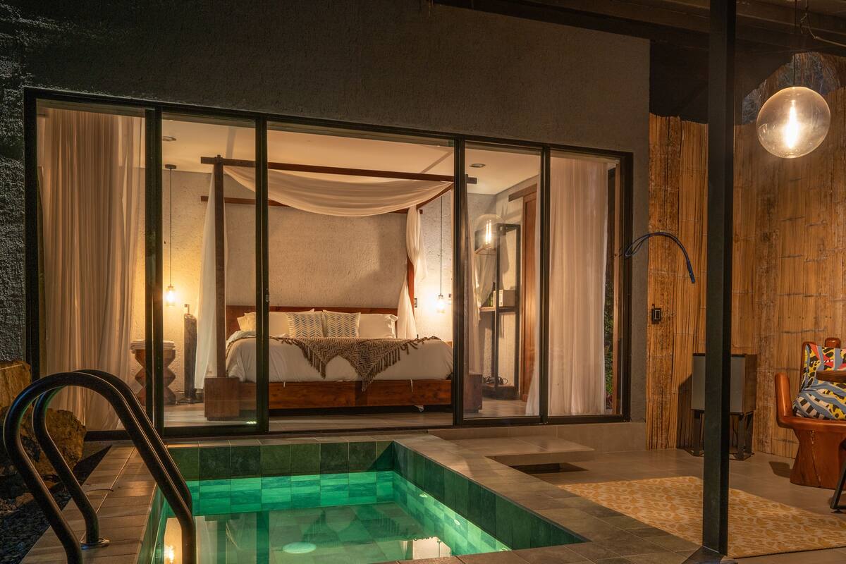 A modern bedroom with a glass door leading to a balcony, a small pool, and a wooden wall.