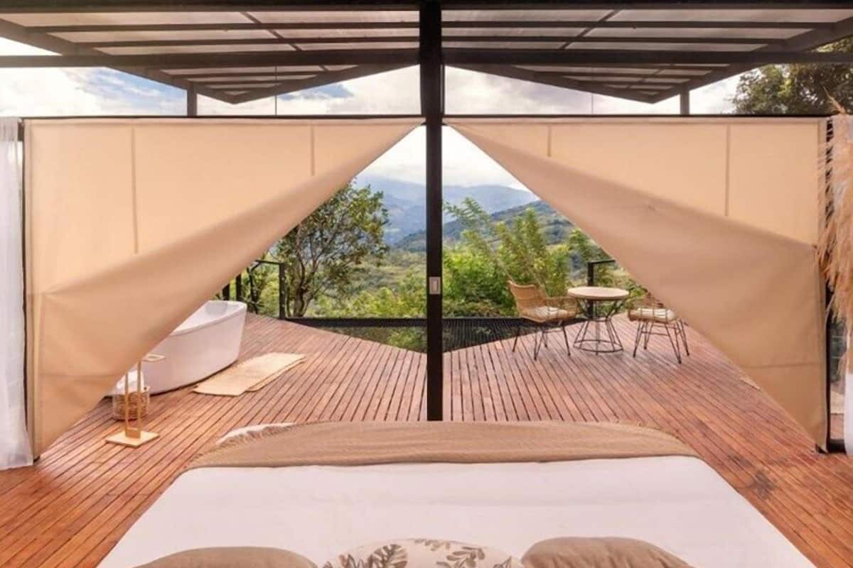 A bedroom with a large bed, wooden flooring, and a view of a patio with outdoor furniture.