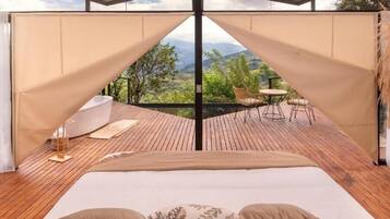 A bedroom with a large bed, wooden flooring, and a view of a patio with outdoor furniture.