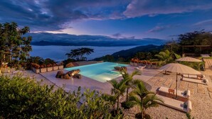 A pool area with lounge chairs and umbrellas, surrounded by greenery and overlooking a mountainous landscape. - Santuario Luxury Ecohotel (Villeta)