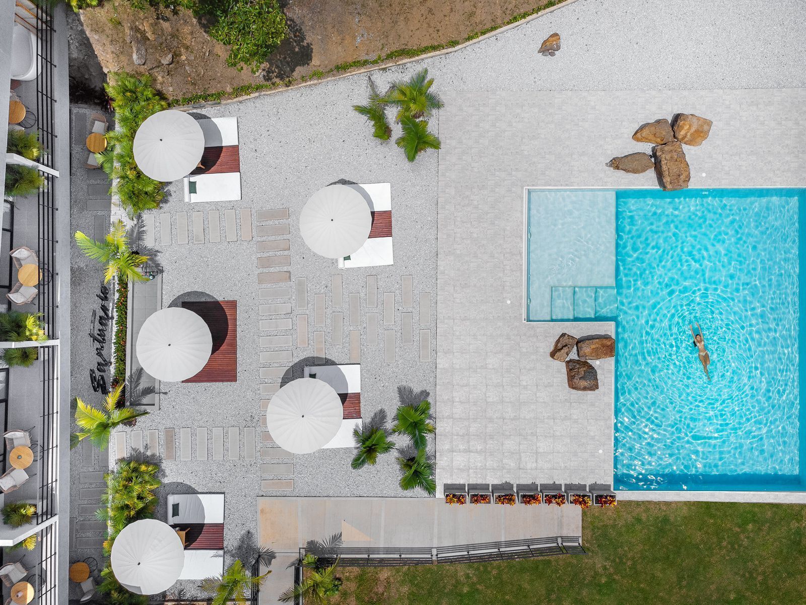 Vista aerea di una zona piscina su un tetto, con diverse poltrone prendisole, ombrelloni e una piscina.