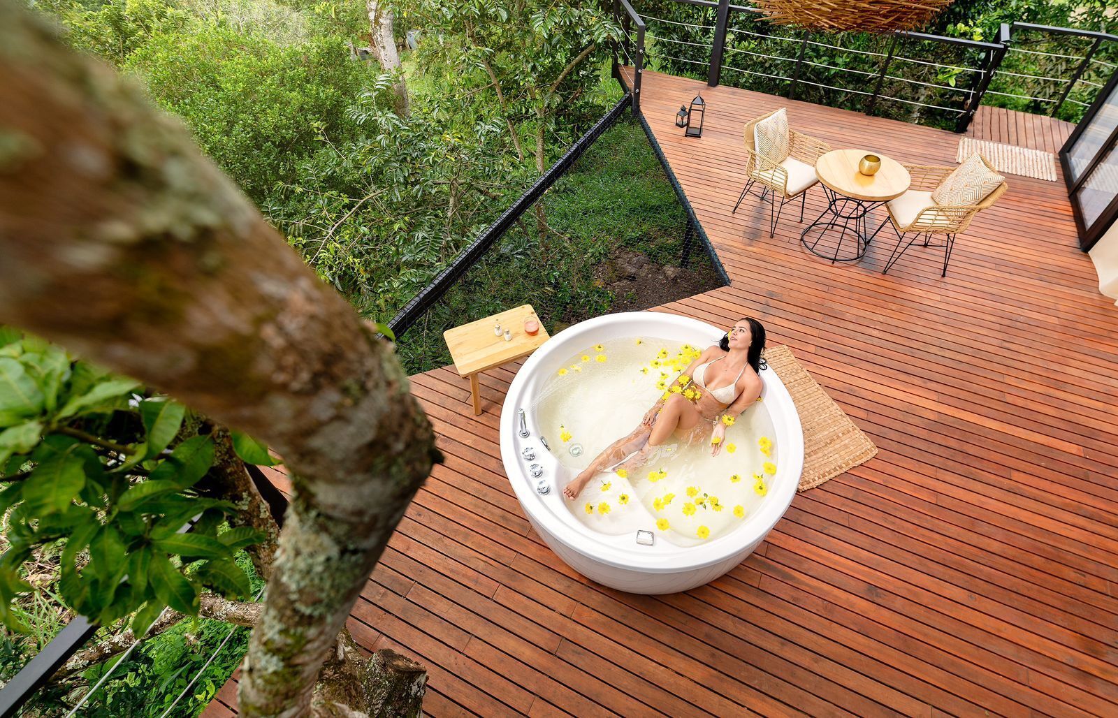 A person relaxing in a hot tub surrounded by a wooden deck, with a view of lush greenery.