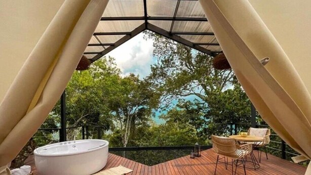 A cozy outdoor deck with a hot tub, wicker furniture, and a view of lush trees. - Santuario Luxury Ecohotel (Villeta)