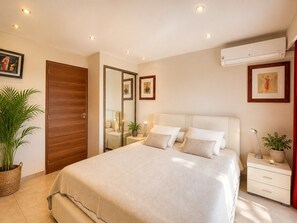 Ein Schlafzimmer mit einem Bett, Nachttischen, einem Spiegel, einer Topfpflanze und einer Klimaanlage.
