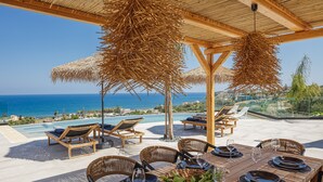 An outdoor dining area with a view of the ocean, wooden furniture, and a table set for a meal. - Villa Zelda - Private Infinity Pool Sea View (Rethymno)