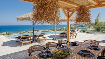 An outdoor dining area with a view of the ocean, wooden furniture, and a table set for a meal.