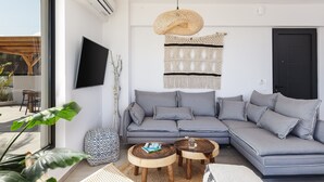 A modern living room with a grey sectional sofa, two wooden coffee tables, a woven pendant light, and a large window with a view of the outdoors. - Villa Zelda - Private Infinity Pool Sea View (Rethymno)