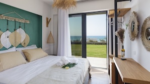 A modern bedroom with a large bed, a view of the sea, and a balcony with a wooden table and decorative mirrors. - Villa Zelda - Private Infinity Pool Sea View (Rethymno)