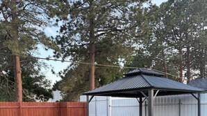 A backyard with a covered patio area, a wooden fence, and a well-maintained lawn. - Casamor - Home in Richland (Richland)